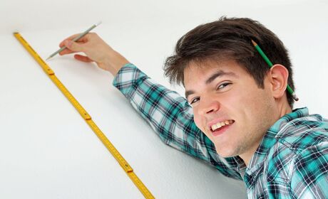Bild Ein lächelnder Techniker misst sorgfältig die Wandhöhe für ein neues Fenster mit einem gelben Maßstab.