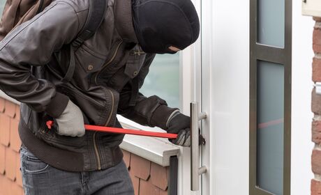 Bild Eine maskierte Person versucht, mit einem Brecheisen eine Haustür aufzubrechen.