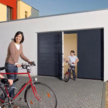 Bild Eine Familie mit Fahrrädern genießt den Tag vor einem modernen Garagentor mit integrierter Tür.