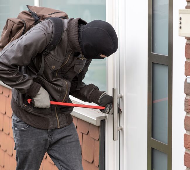 Bild Eine maskierte Person versucht, mit einem Brecheisen eine Haustür aufzubrechen.